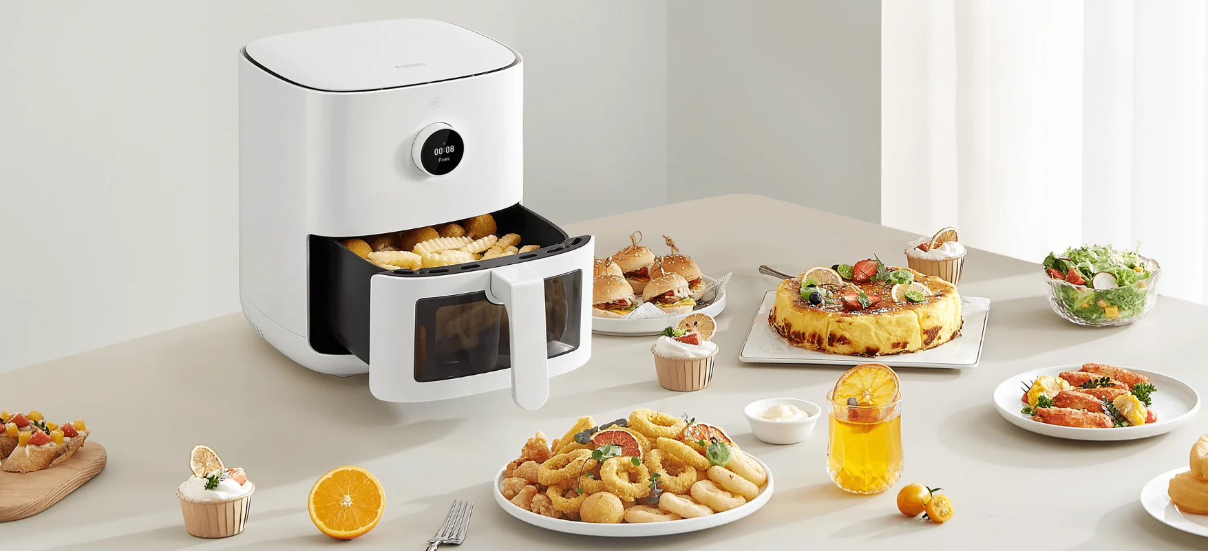 Une friteuse à air Xiaomi Smart Air Fryer 4L Pro blanche sur un comptoir de cuisine, avec son tiroir ouvert révélant des aliments en train de cuire. Autour, une variété de plats appétissants : beignets, burgers, gâteaux, salades et crevettes, illustrant la polyvalence de l'appareil pour une cuisine saine et savoureuse.